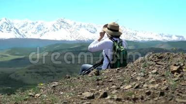 那个带着绿色背包的旅行者的女人坐着看雪山。 鹰在天空中飞翔。